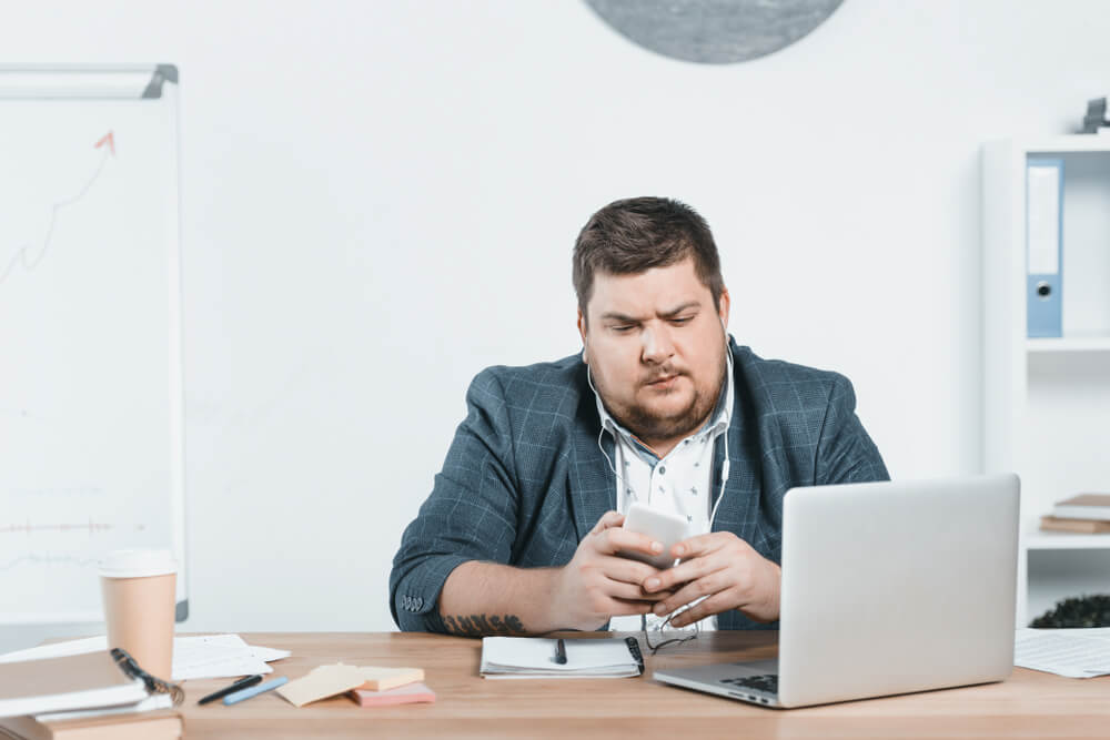 Overweight,Businessman,Listening,Music,With,Smartphone,While,Using,Laptop,At Prof Michael Talbot